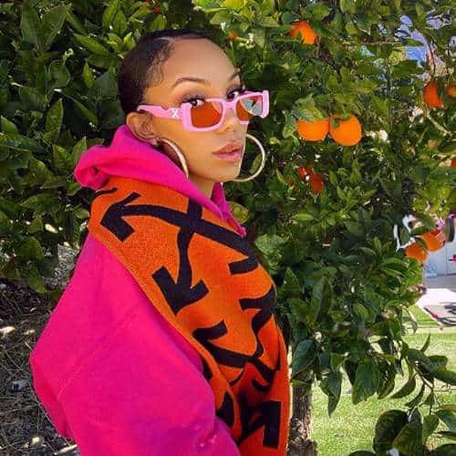 Alyssa wearing pink shade and pink hoody standing under an orange tree