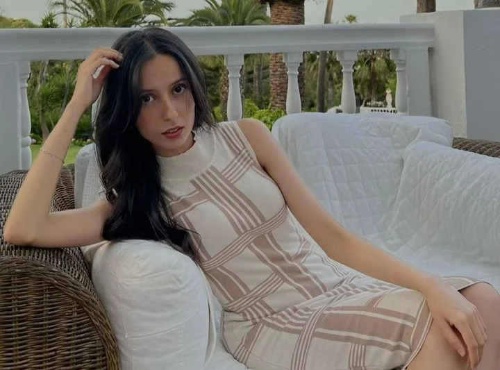 Fatima El Bakkali Kasmi chilling on patio sofa with palm trees in the background