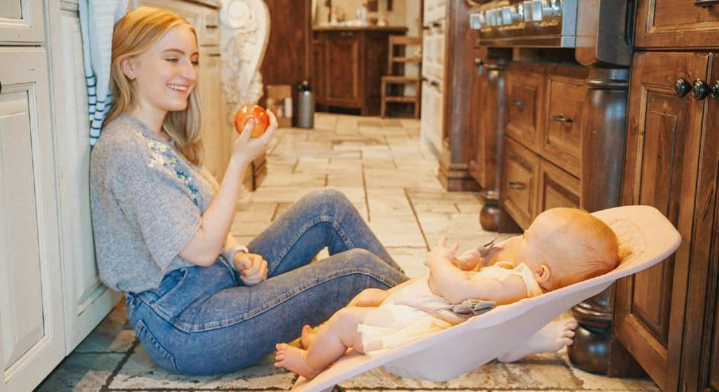 Hannah Uhl sitting on kitchen floor with baby about to eat apple