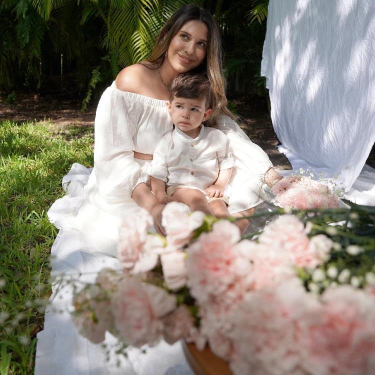 Jeniffer Diaz and her son sitting on the grass with pink roses in foreground