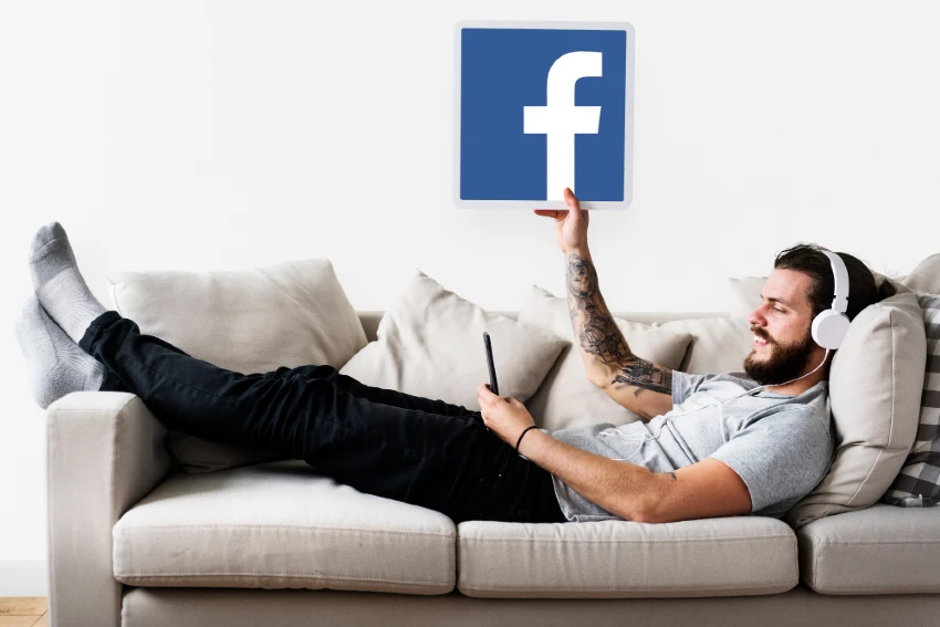 Man lying on the sofa while holding up a Facebook sign | Reviewing marketing strategies