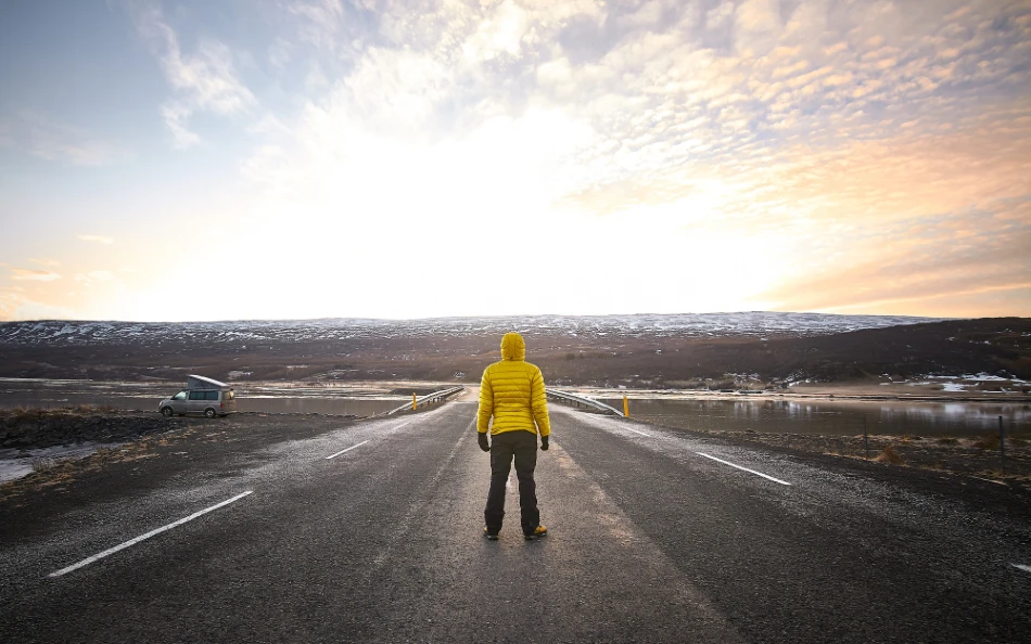 Man in yellow jacket on open road watching the sunset