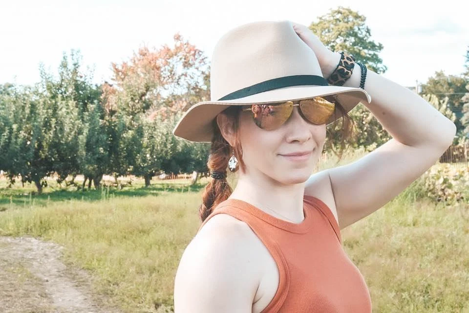 Sarah Ballard wearing sunglasses and holding her hat in a field