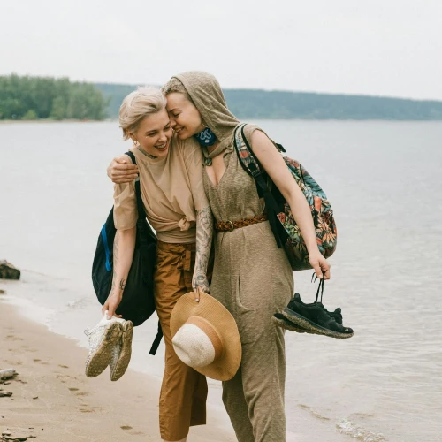 Two women carrying their shoes on the beach embrace each other